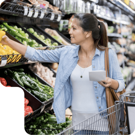 Una mujer escogiendo verduras en el supermercado con su carrito al lado.