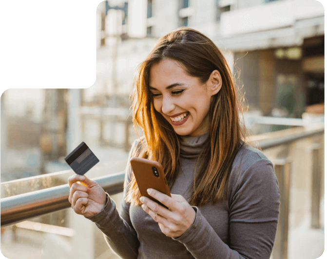 Una mujer sonriendo mientras sostiene su celular y su tarjeta de crédito.